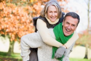 Senior man giving woman piggyback ride through autumn woods